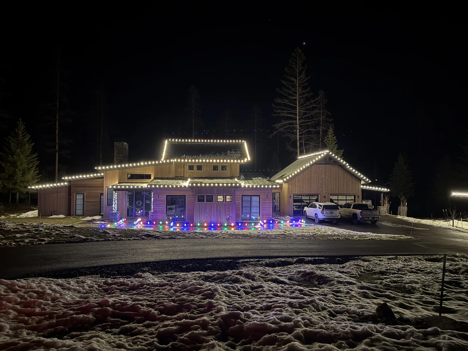 A Flathead Valley home with warm-white C9 lights tracing every roofline at night, snow on the ground