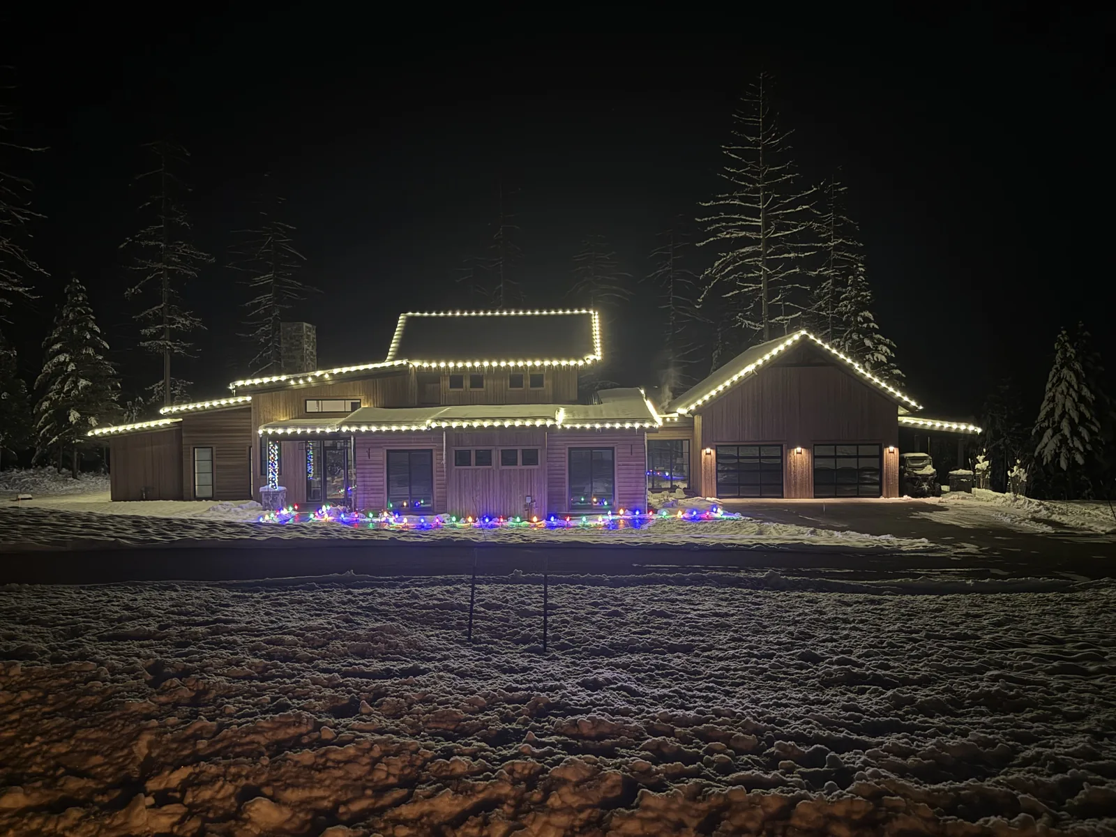 The same warm-white roofline install viewed from a second angle at night, snow-covered driveway in the foreground