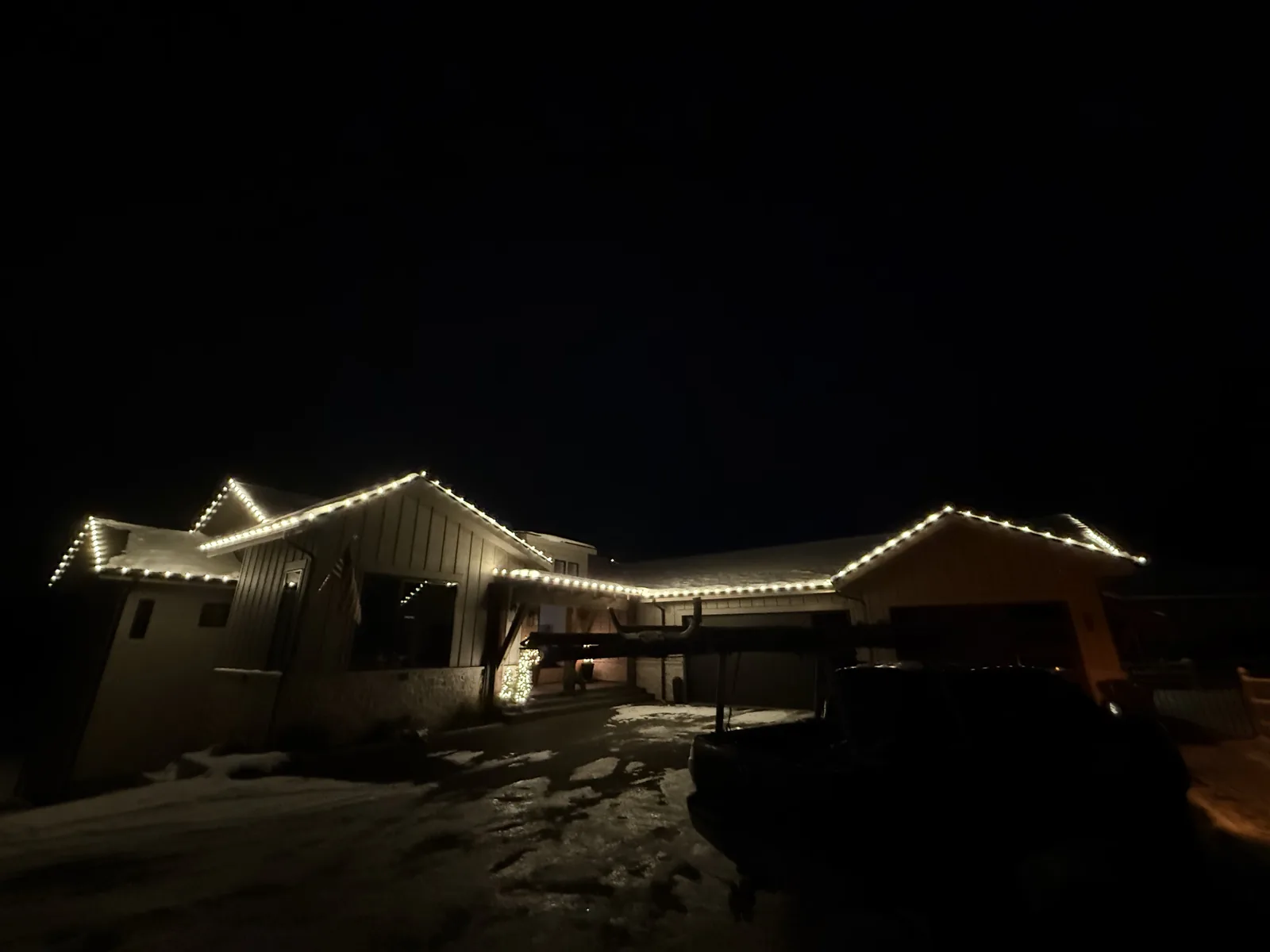 A modern multi-gable home with clean warm-white lines along every roof edge, photographed at night against dark pines