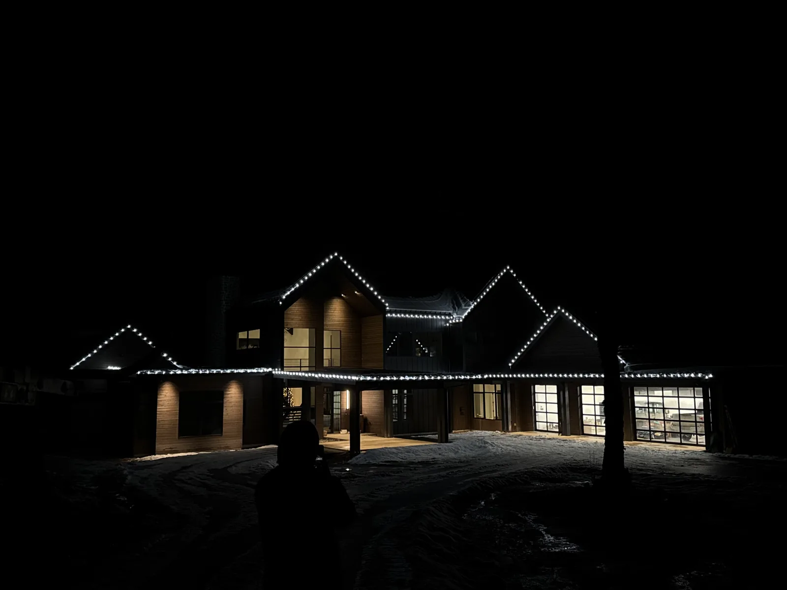 A large two-story home with several gables outlined in warm-white lights at night, garage doors lit from inside